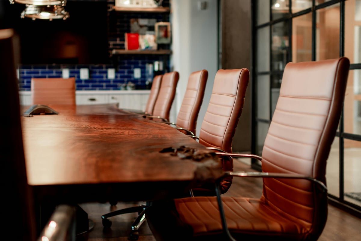 A long wooden boardroom table lined with brown leather chairs in a modern office