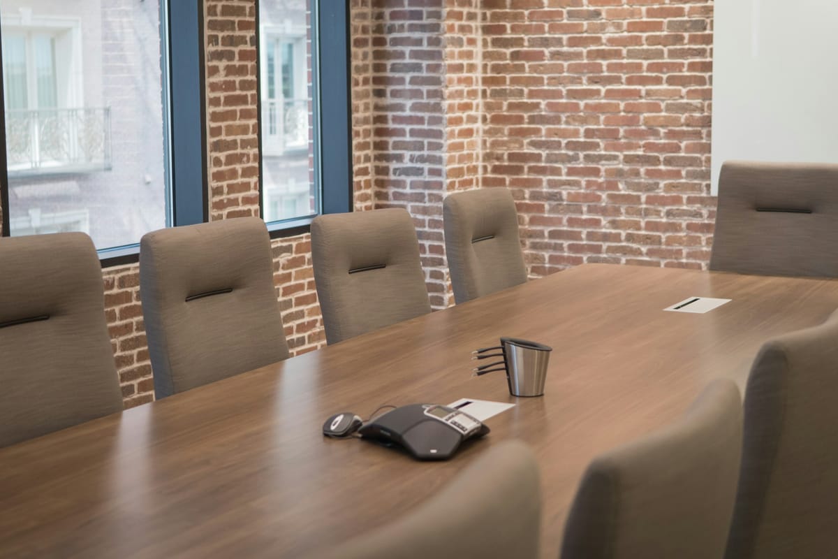 A meeting room with brick walls, a wooden table and a conference speakerphone in the middle