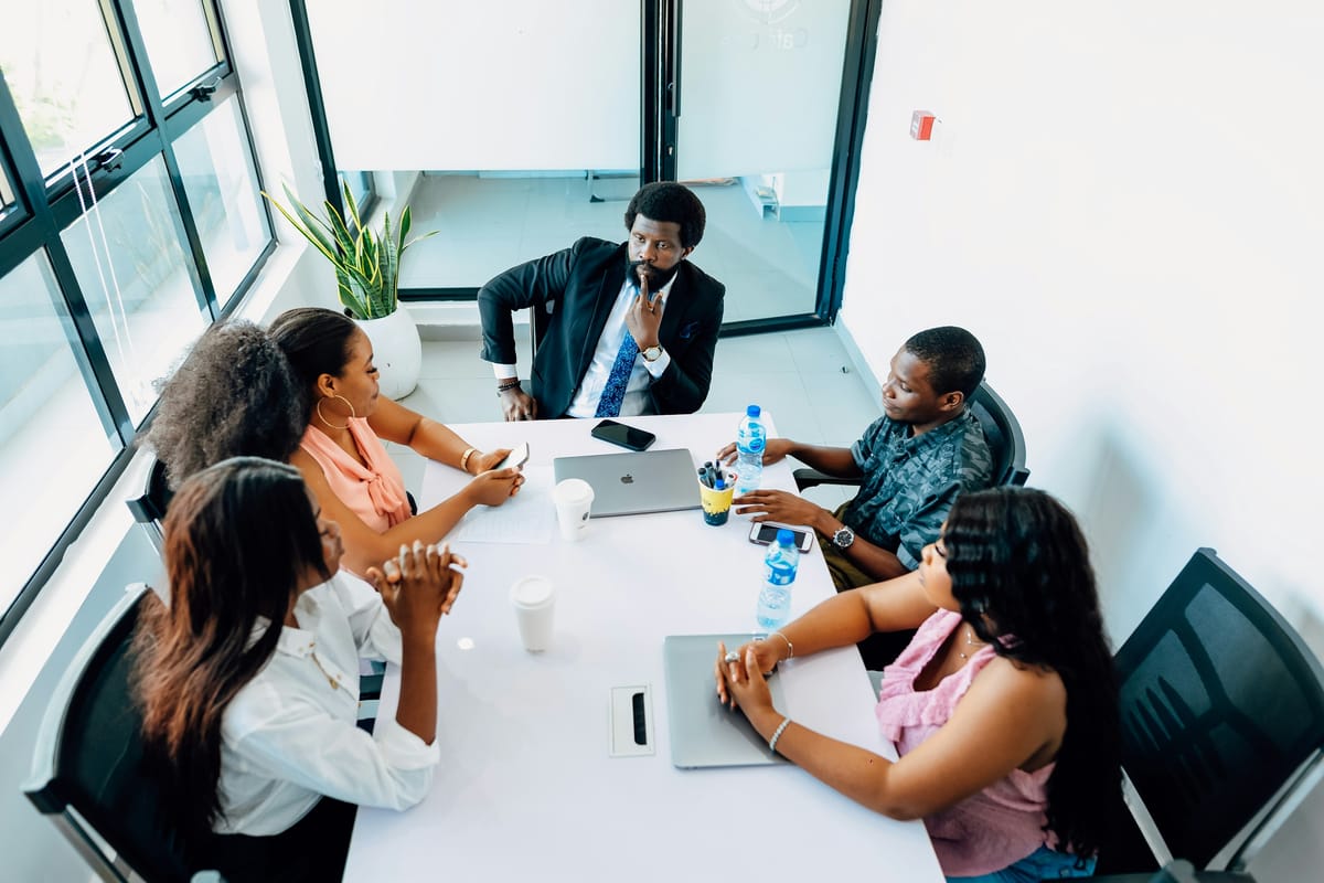 Seen from above, six people around a white meeting table with laptops and water bottles, mid discussion