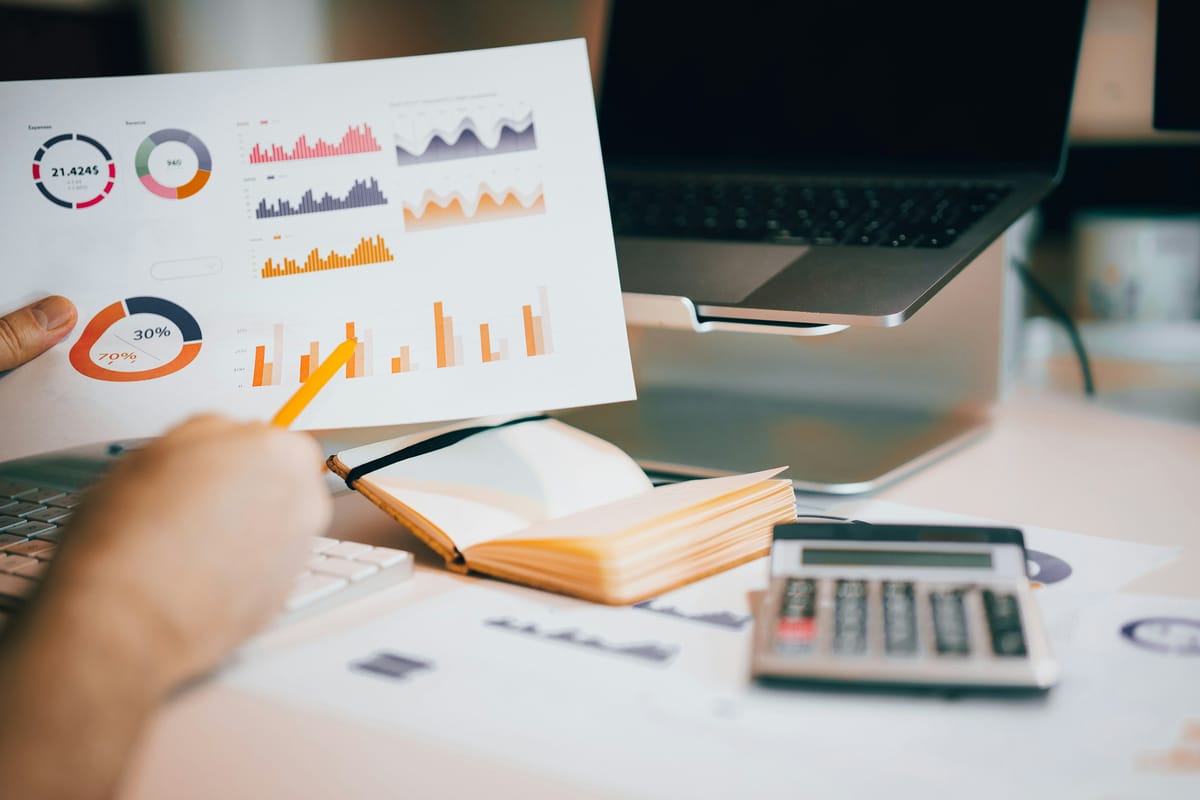 A printed report with bar charts and donut charts, a pencil pointing at one figure, and a calculator beside it