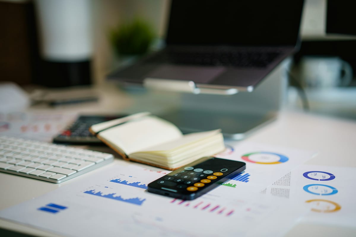 A desk with printed charts, a phone calculator, an open notebook and a keyboard