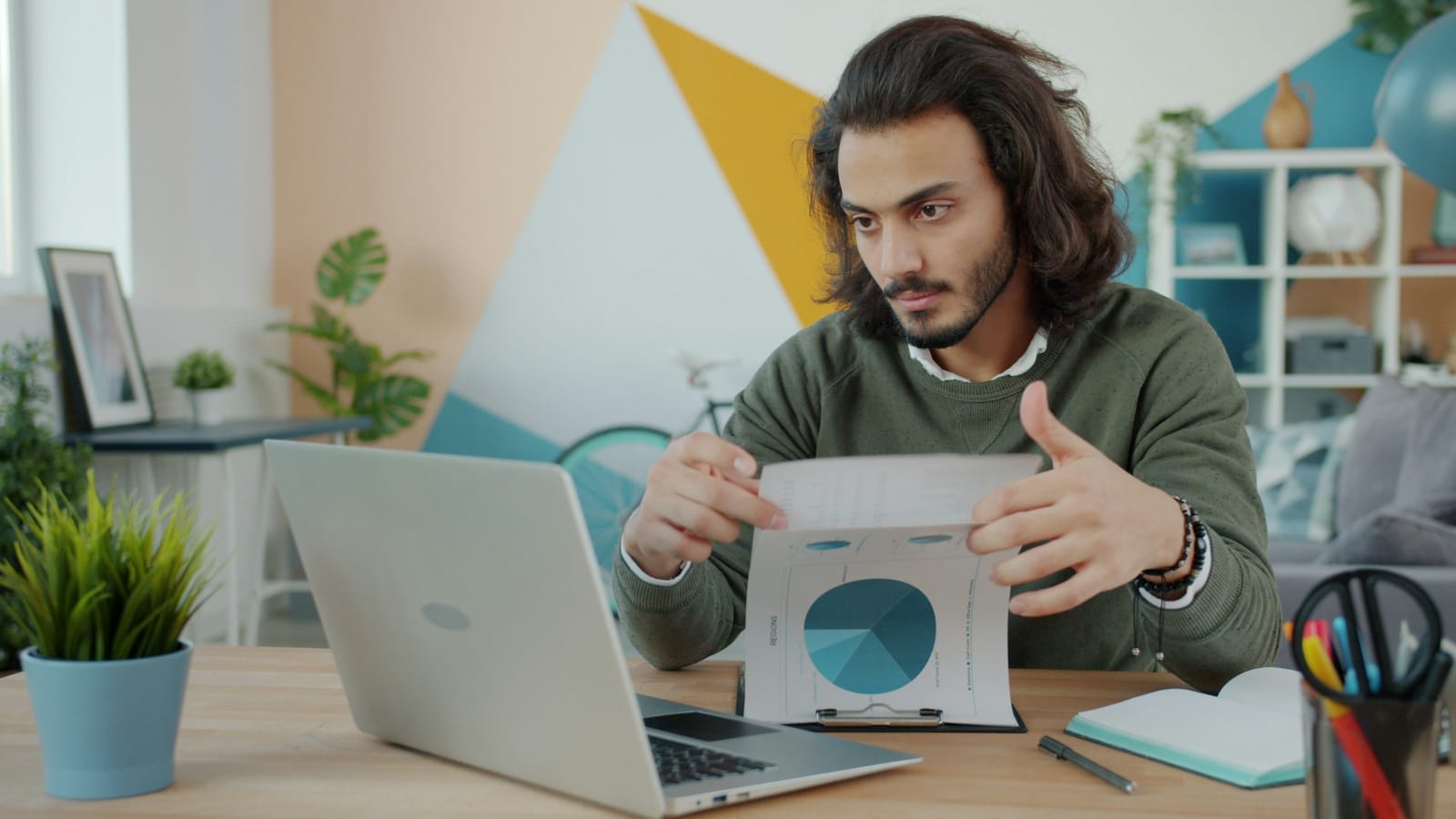 A young founder at a desk with a laptop, studying a printed pie chart