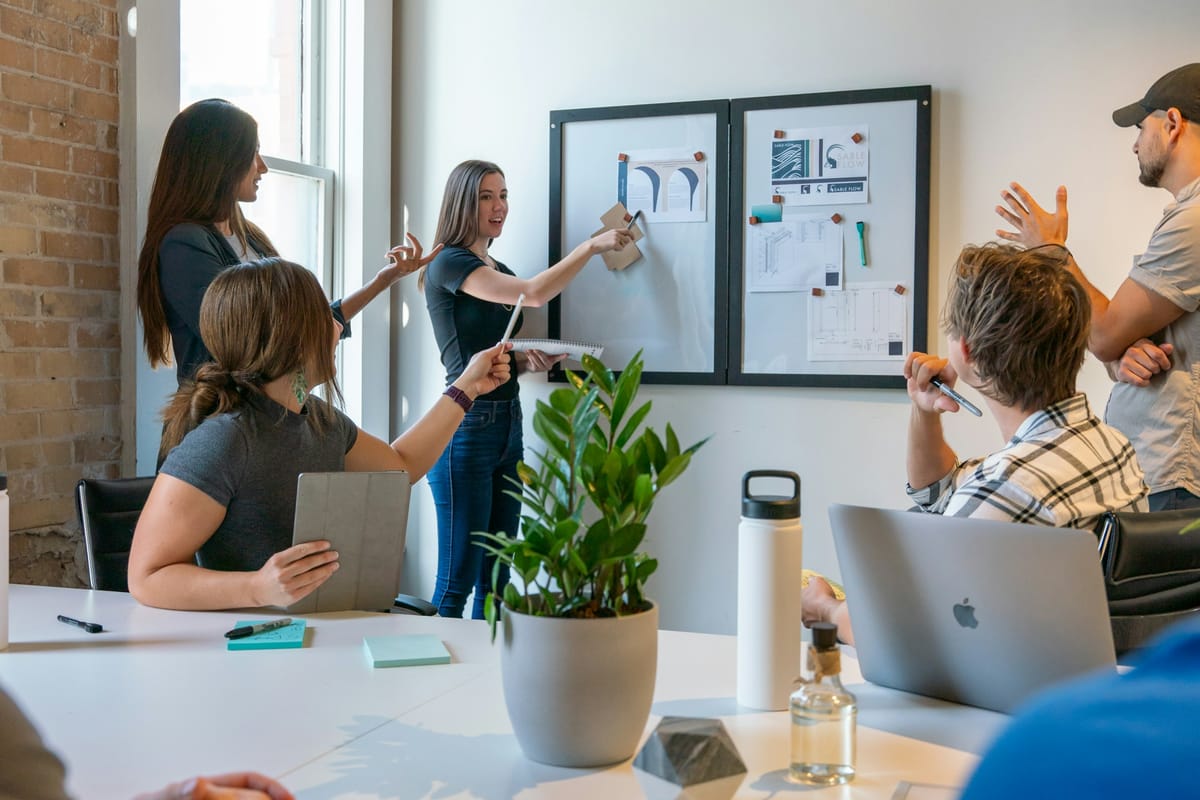 A small startup team in a bright office, one person pointing at notes pinned to a board while others discuss