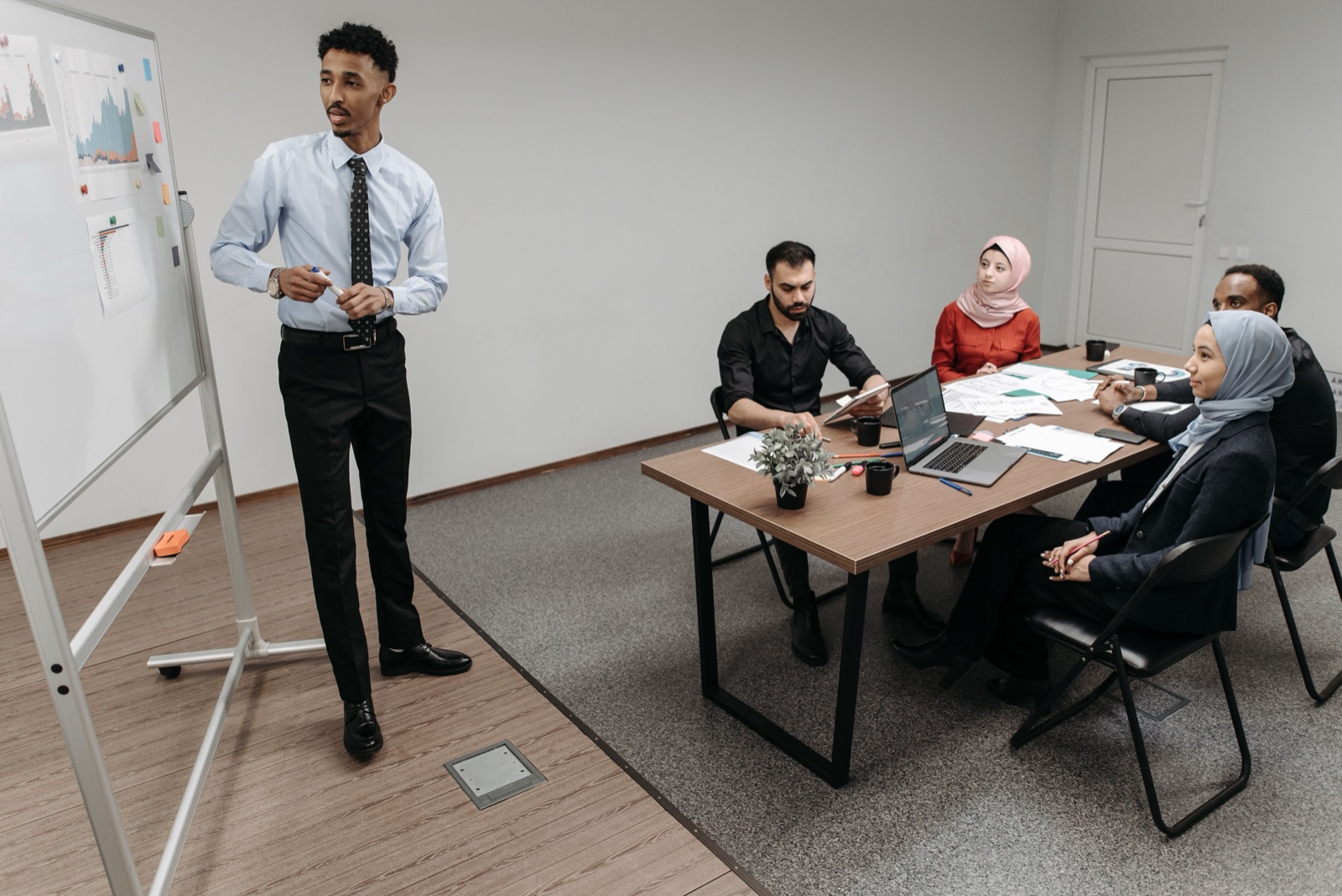 A person presenting graphs on a whiteboard to a small group of colleagues